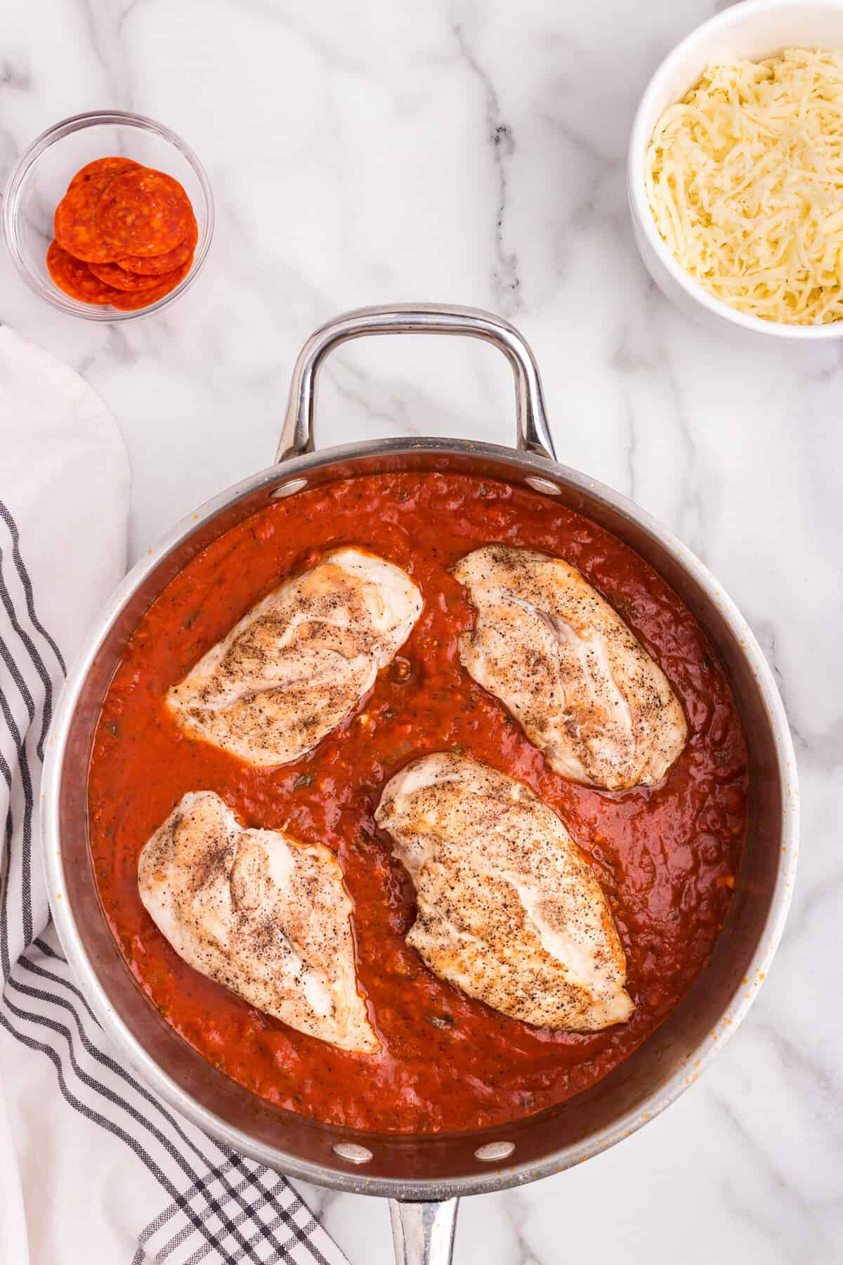 Overhead picture of chicken breast in pizza sauce in a pan.