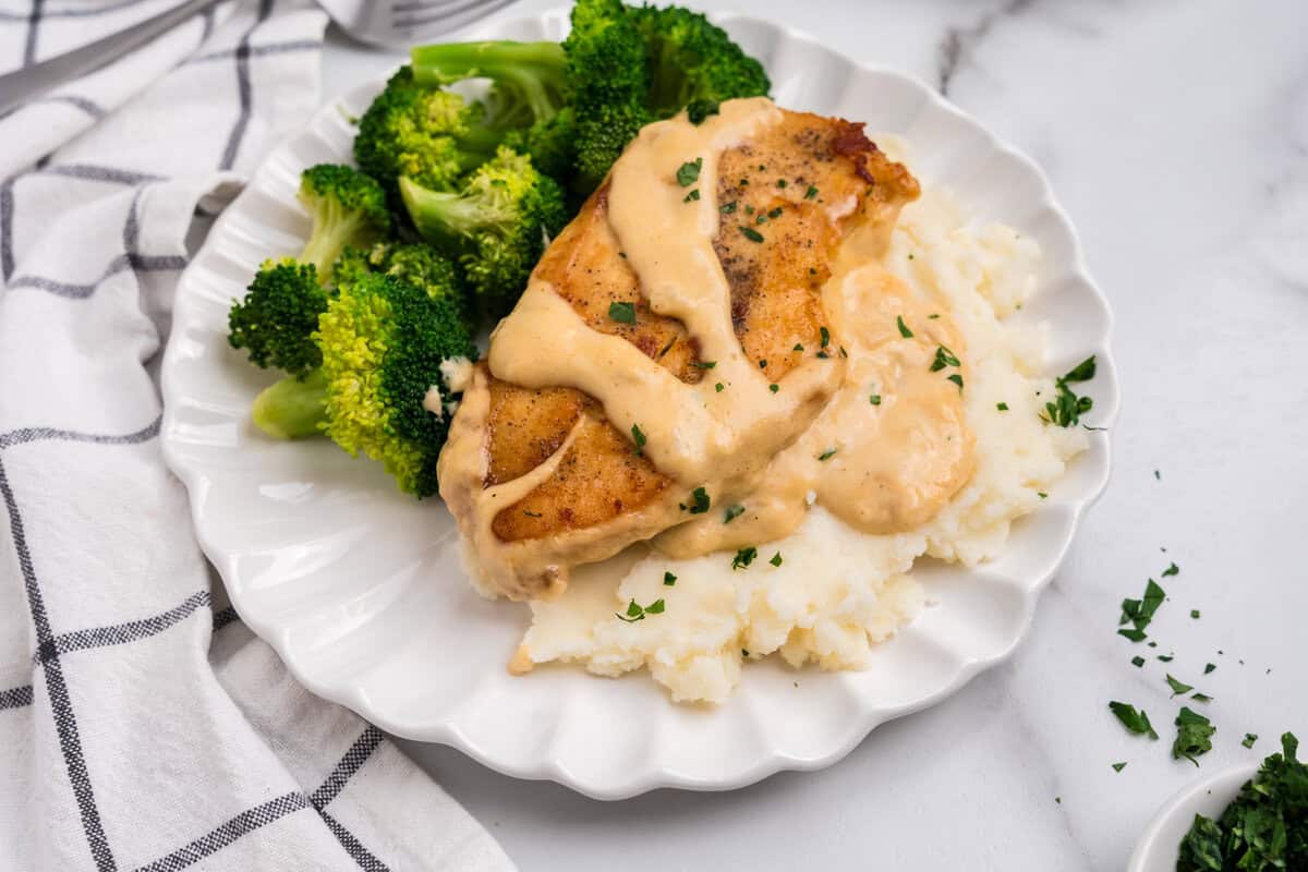 Close up picture of white plate with smothered chicken, mashed potatoes and broccoli on it.