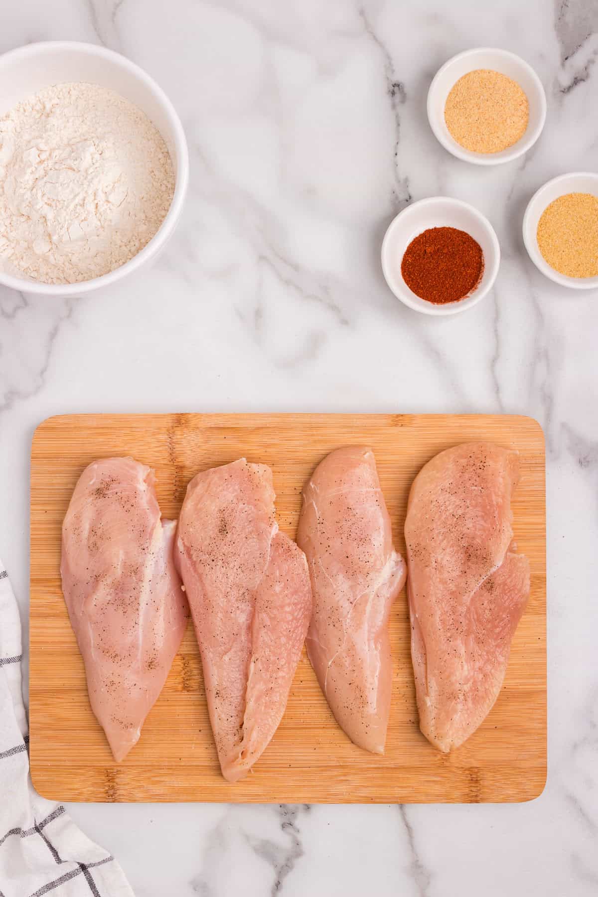 Overhead picture of raw chicken breast on a wooden cutting board with other ingredients in the background.