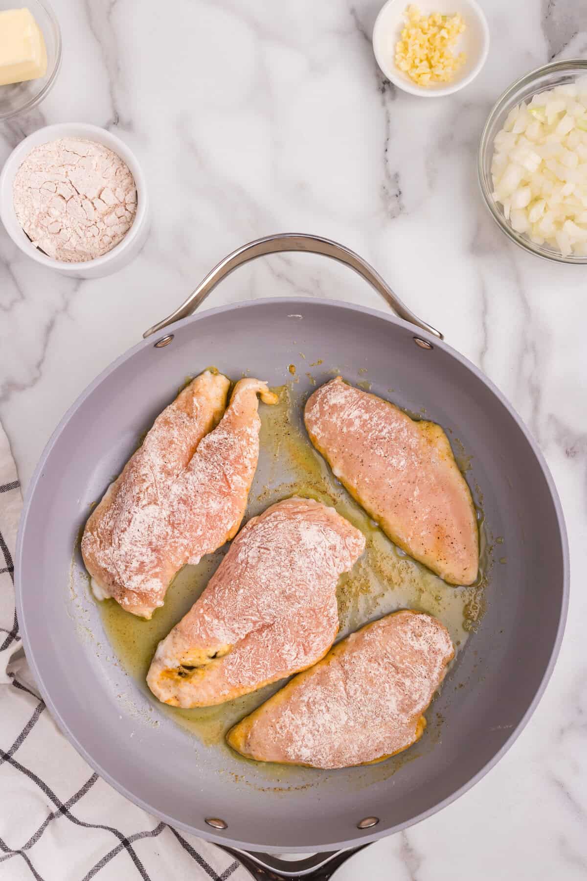 Overhead picture of raw chicken cooking in a frying pan.