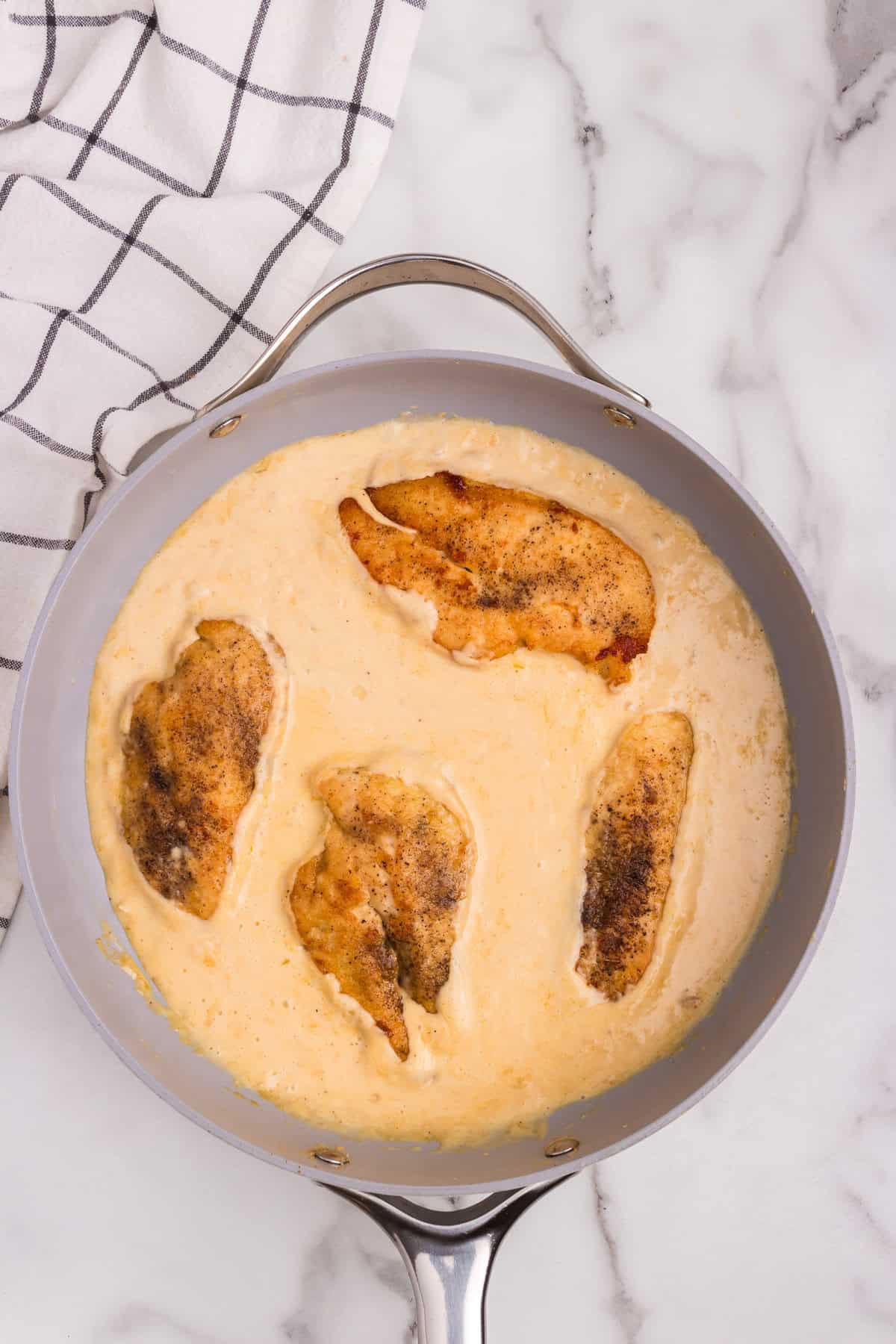 Overhead picture of smothered chicken cooking in a frying pan.
