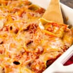 White baking dish with wooden spoon scooping meatball stuffed shells