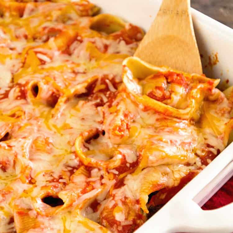 White baking dish with wooden spoon scooping meatball stuffed shells