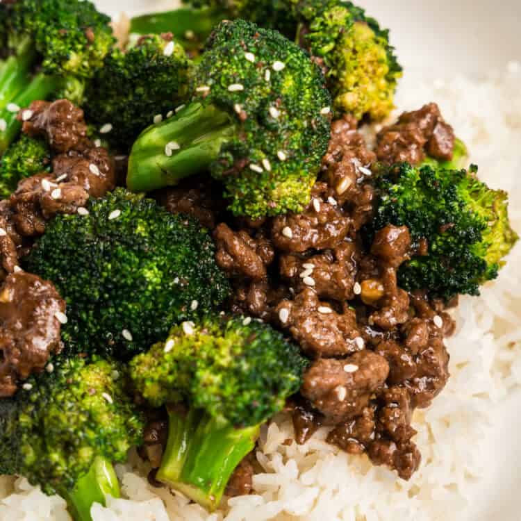 A close-up of a bowl filled with white rice, topped with ground beef and broccoli coated in a savory sauce, and garnished with sesame seeds. The dish is vibrant with bright green broccoli and rich, flavorful beef.