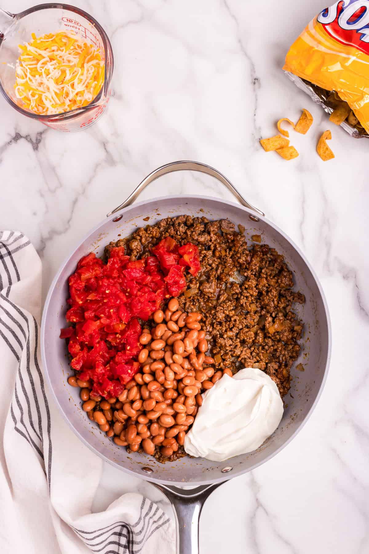 Overhead picture of cooked meat, beans, rotel and sour cream uncombined in pan.