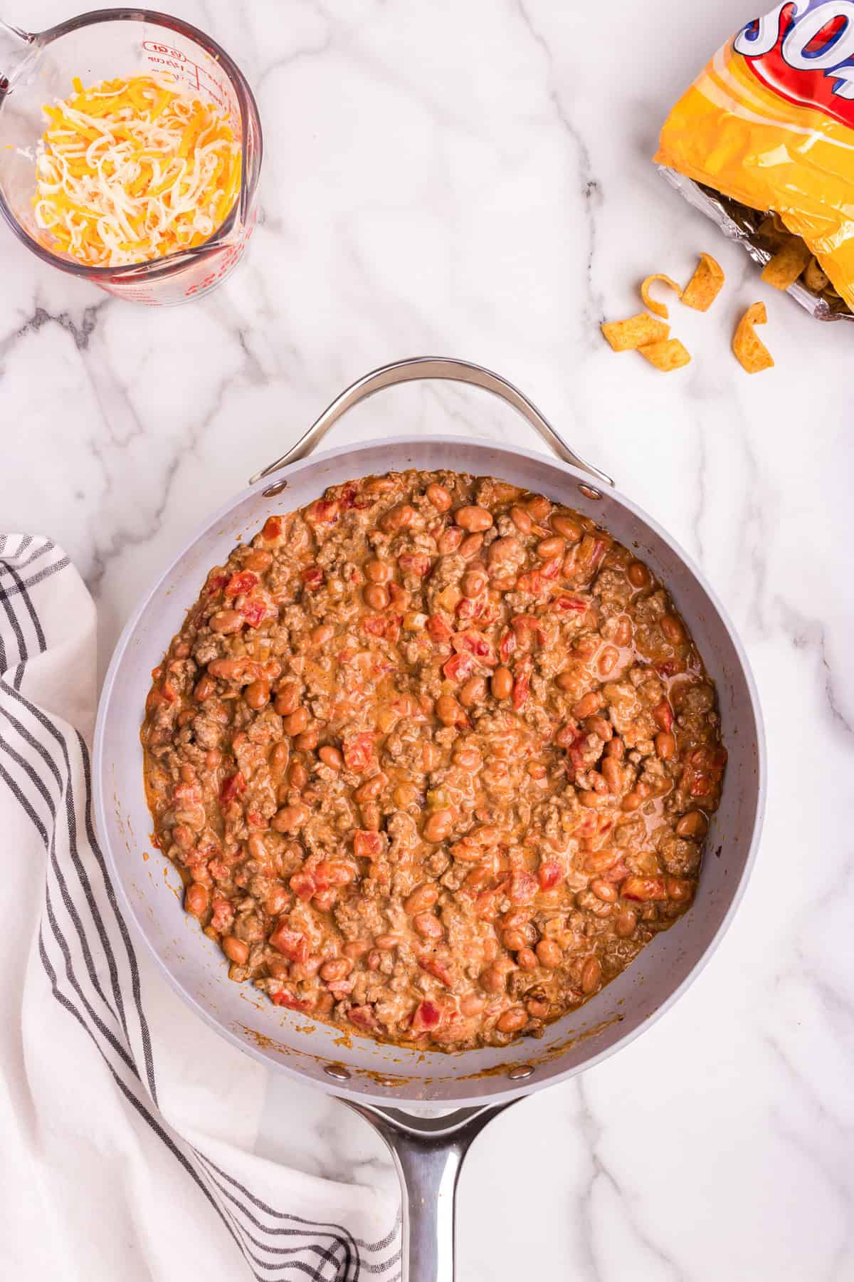 Overhead picture of cooked meat, beans, rotel and sour cream combined in pan.
