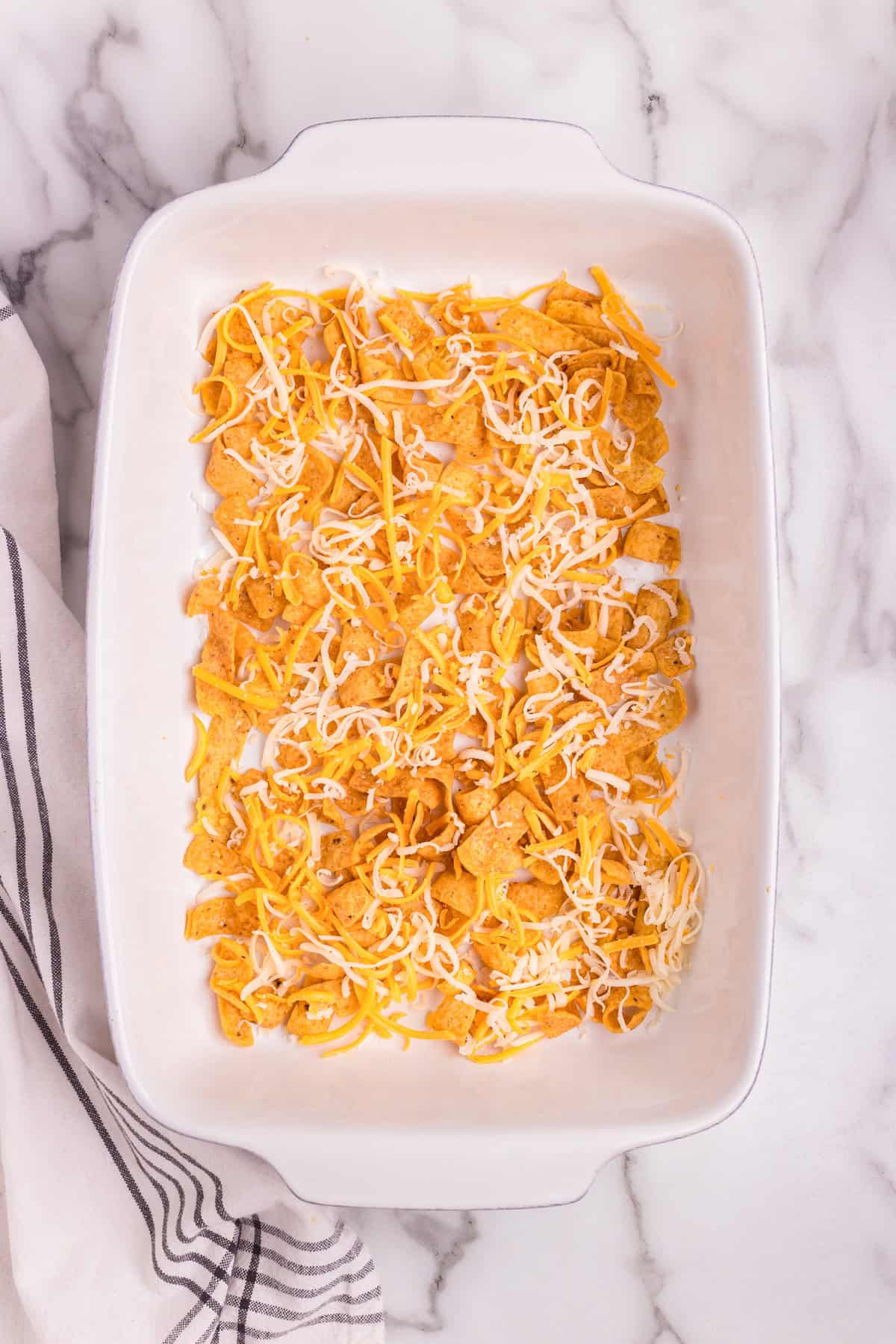 Overhead picture of Frito chips and cheese in the bottom of white baking dish.