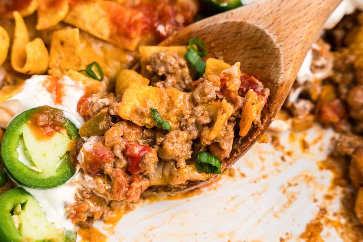 Close up picture of completed walking taco casserole being scooped out of a baking dish with a wooden spoon.