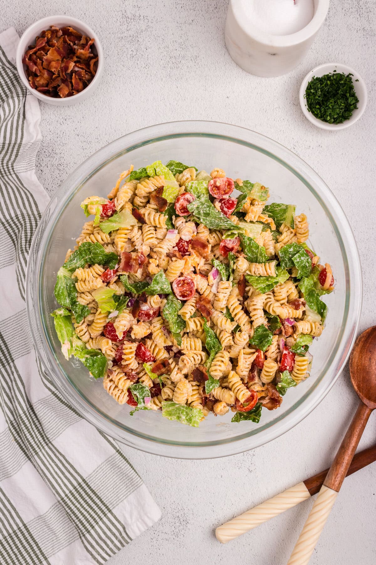 Overhead view of a finished BLT pasta salad in a glass bowl, featuring rotini pasta, cherry tomatoes, chopped romaine lettuce, crispy bacon, red onion, and creamy dressing, ready to serve.