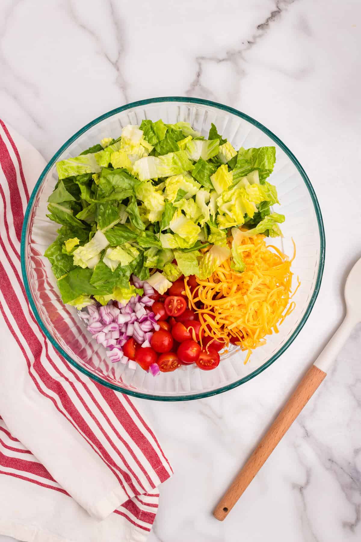 Fresh romaine lettuce, cherry tomatoes, shredded cheddar, and chopped red onions have been added to the bowl with the dressing, not yet mixed.