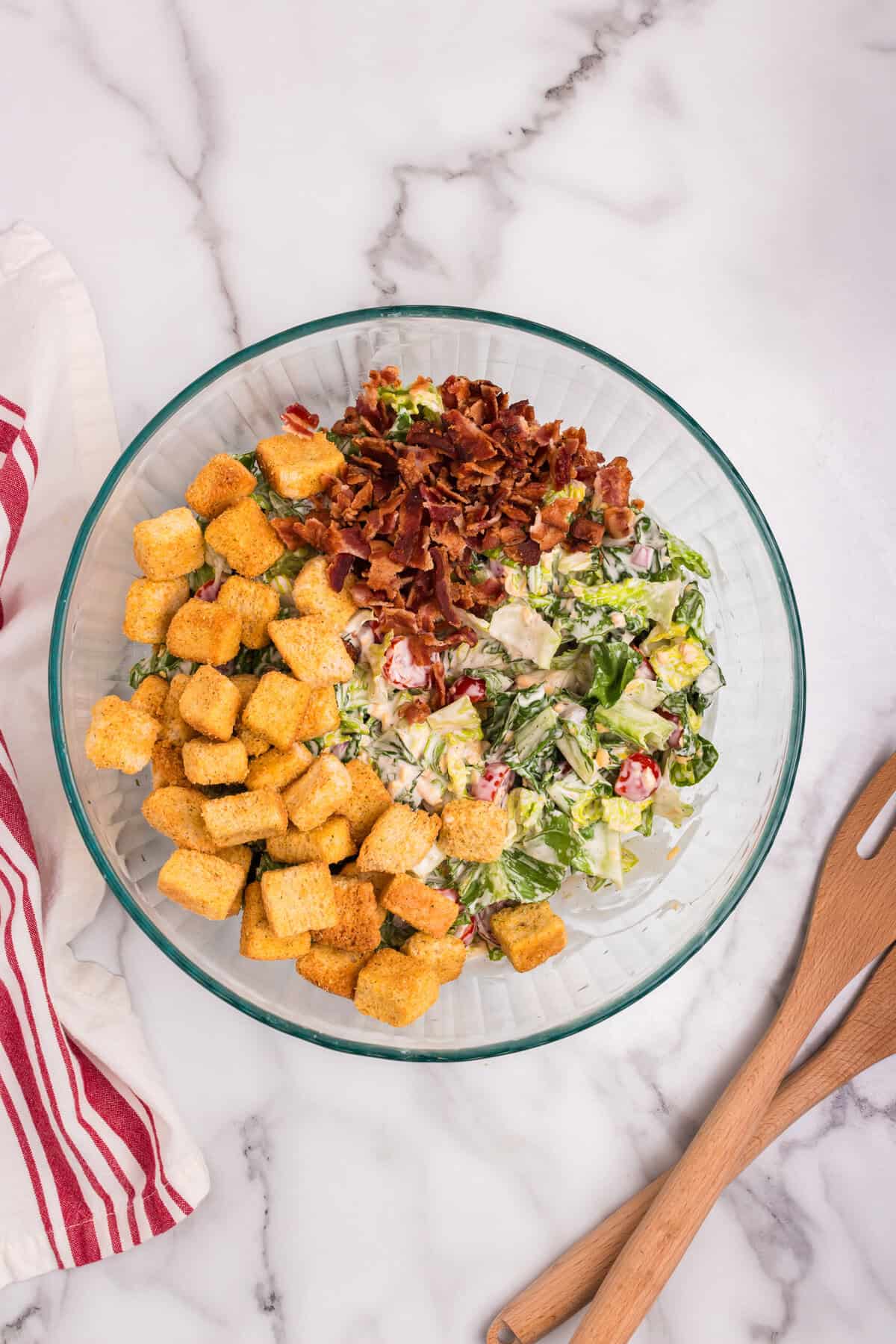 Crumbled bacon and seasoned croutons have been added on top of the mixed salad in the glass bowl.
