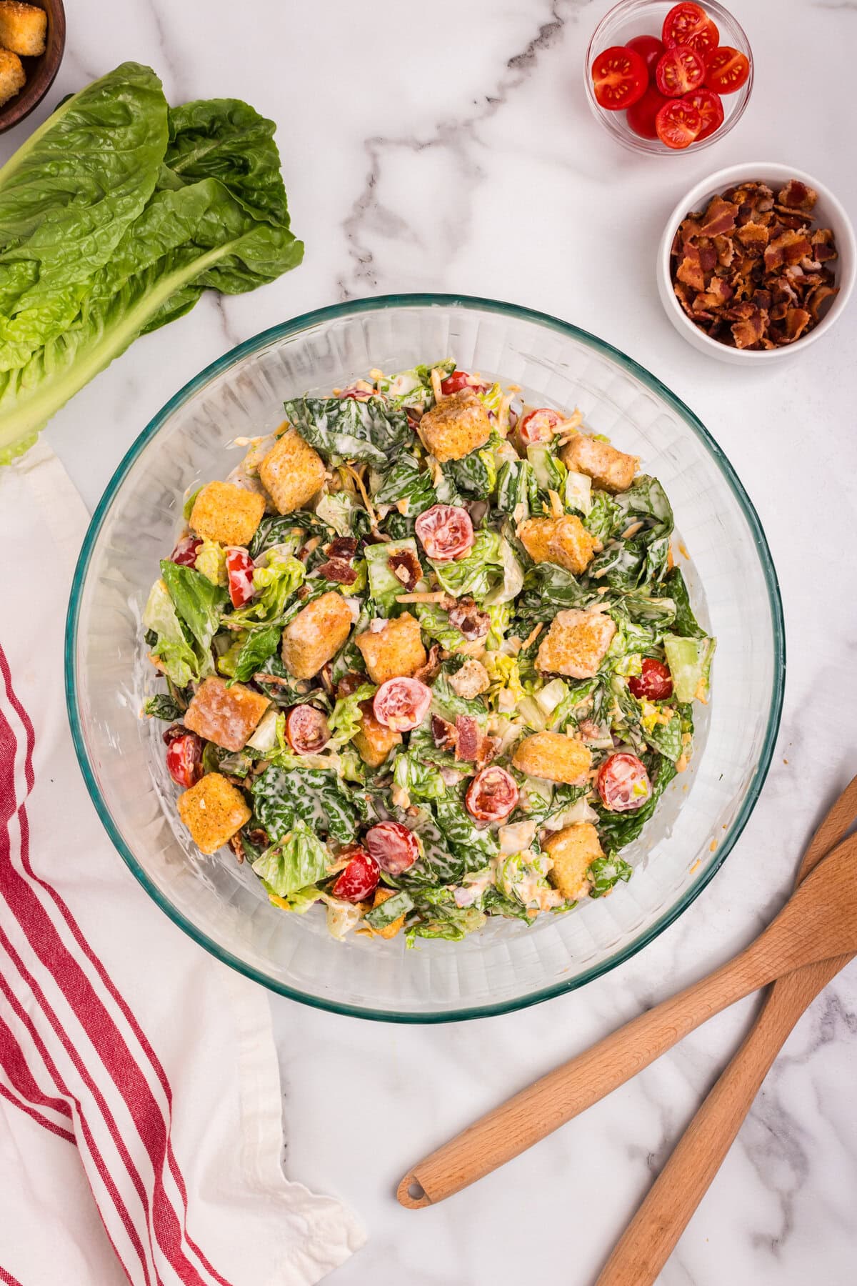 The final salad is fully combined, showcasing colorful ingredients: romaine, tomatoes, croutons, bacon bits, cheddar, and creamy dressing.