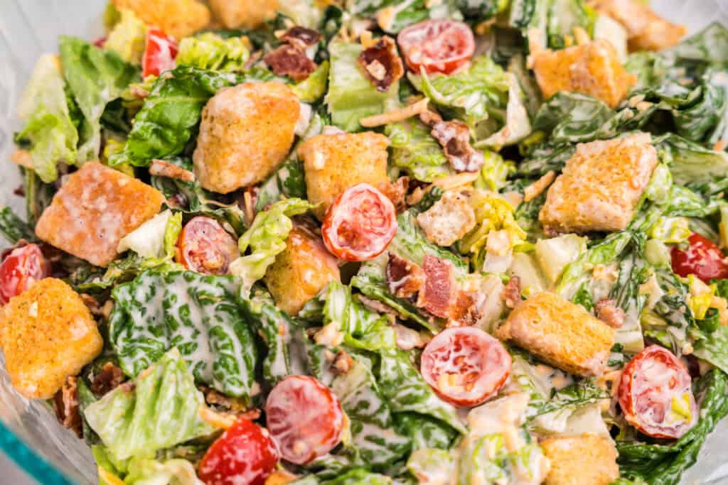 An even closer macro shot of the BLT salad, highlighting juicy cherry tomato halves, crunchy croutons, bits of bacon, and creamy-coated romaine leaves.