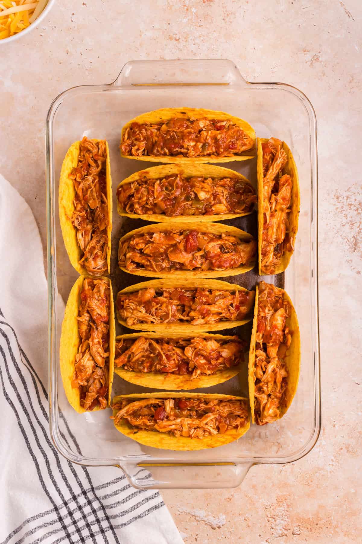 The taco shells in the baking dish are filled with the cooked chicken mixture.