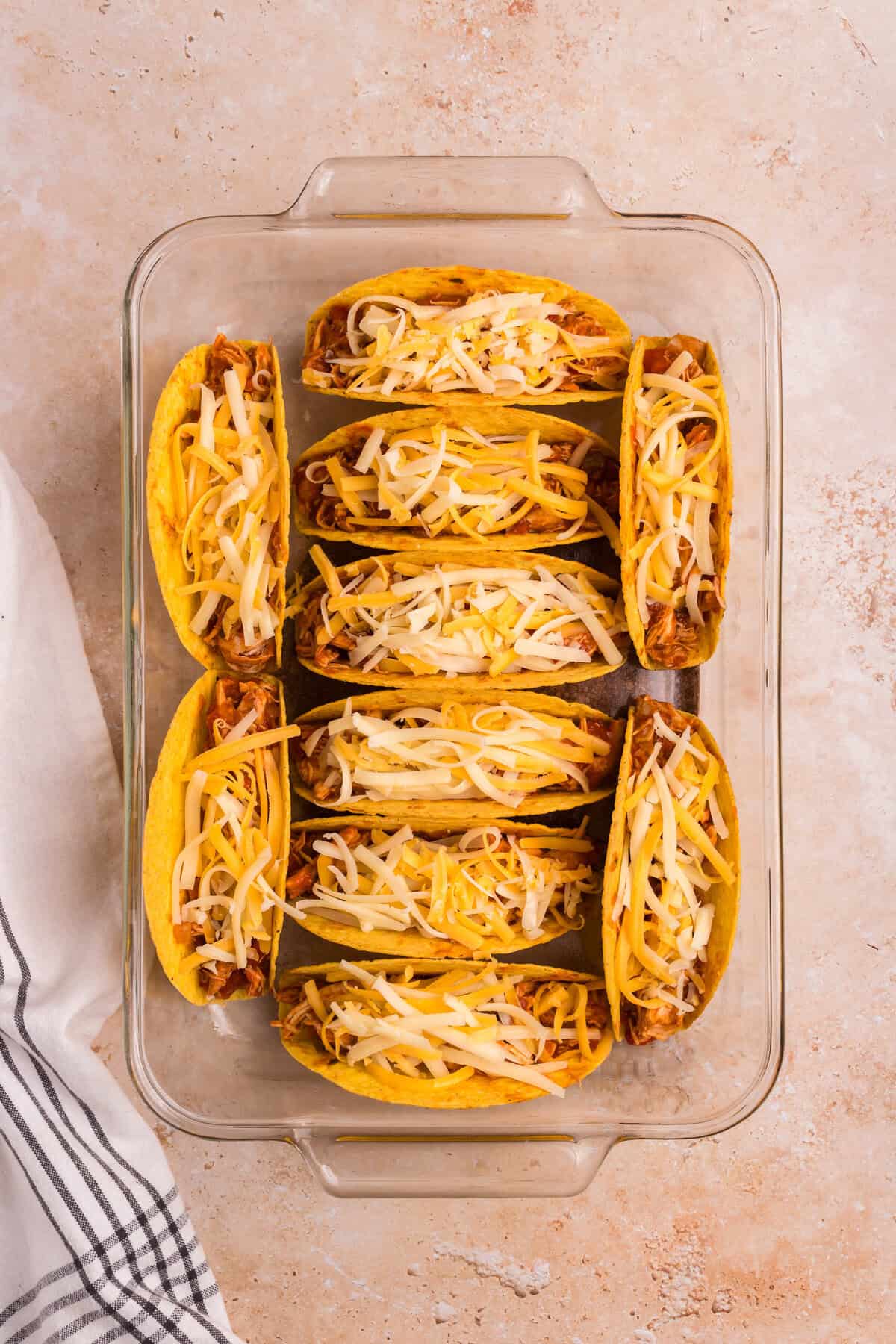 Shredded cheese has been added on top of the filled tacos, ready for baking.