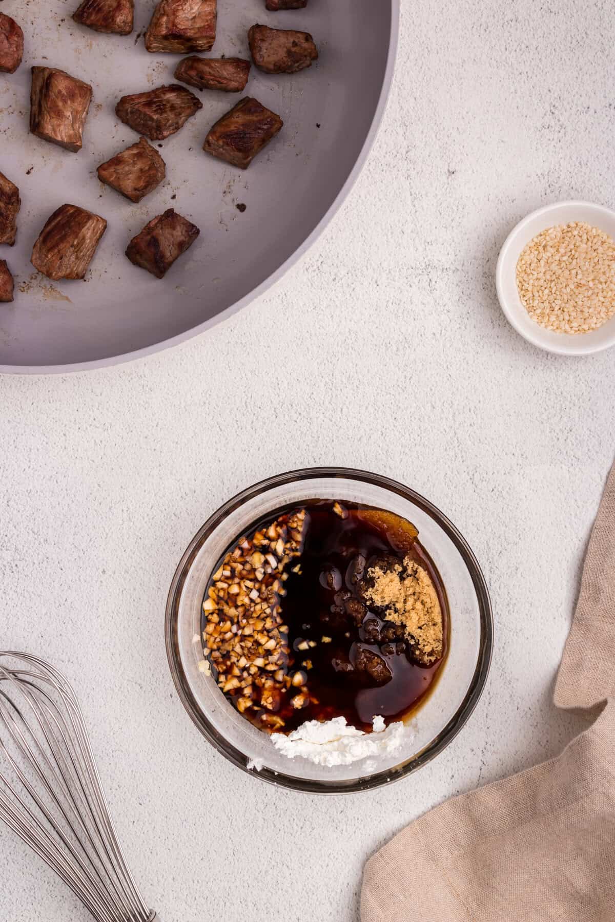 A glass bowl with separated sauce ingredients including minced garlic, soy sauce, brown sugar, and cornstarch, positioned near the skillet.