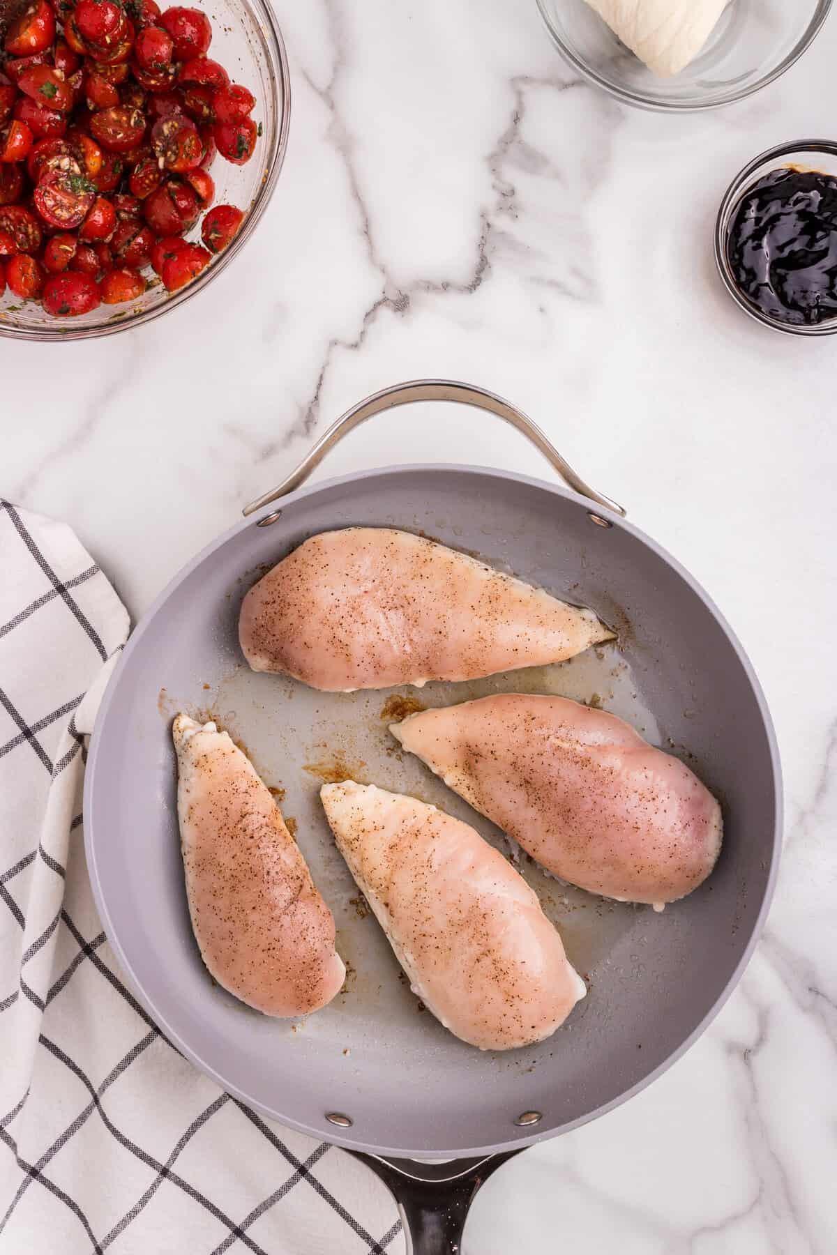 Raw chicken breasts are seasoned and placed in a skillet, ready to be cooked.