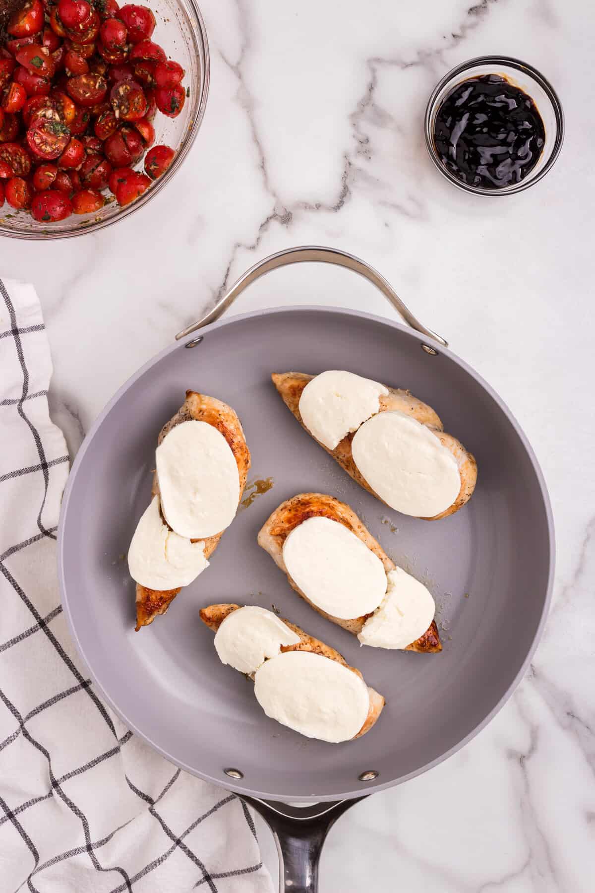 Slices of fresh mozzarella are placed on top of the seared chicken breasts in the skillet.