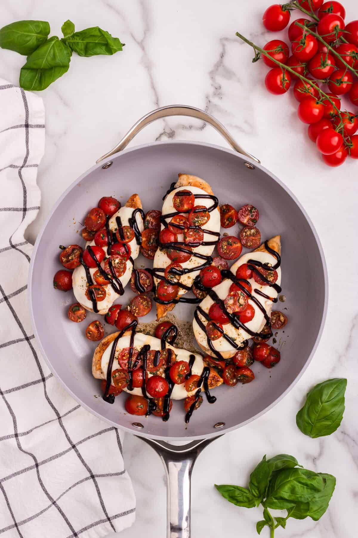 The final dish is garnished with a drizzle of balsamic glaze and fresh basil leaves around the pan—Bruschetta Chicken is ready to serve.
