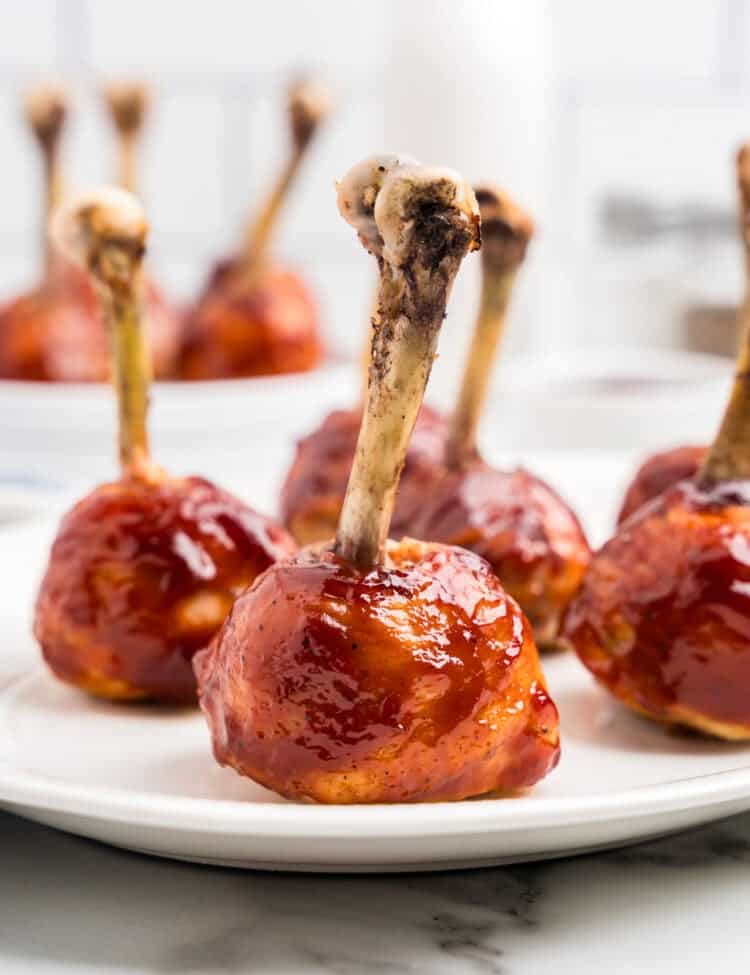 Plate of glazed chicken lollipop drumsticks with a shiny barbecue coating.