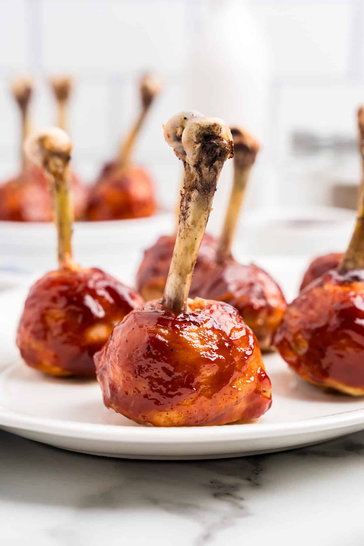 Plate of glazed chicken lollipop drumsticks with a shiny barbecue coating.