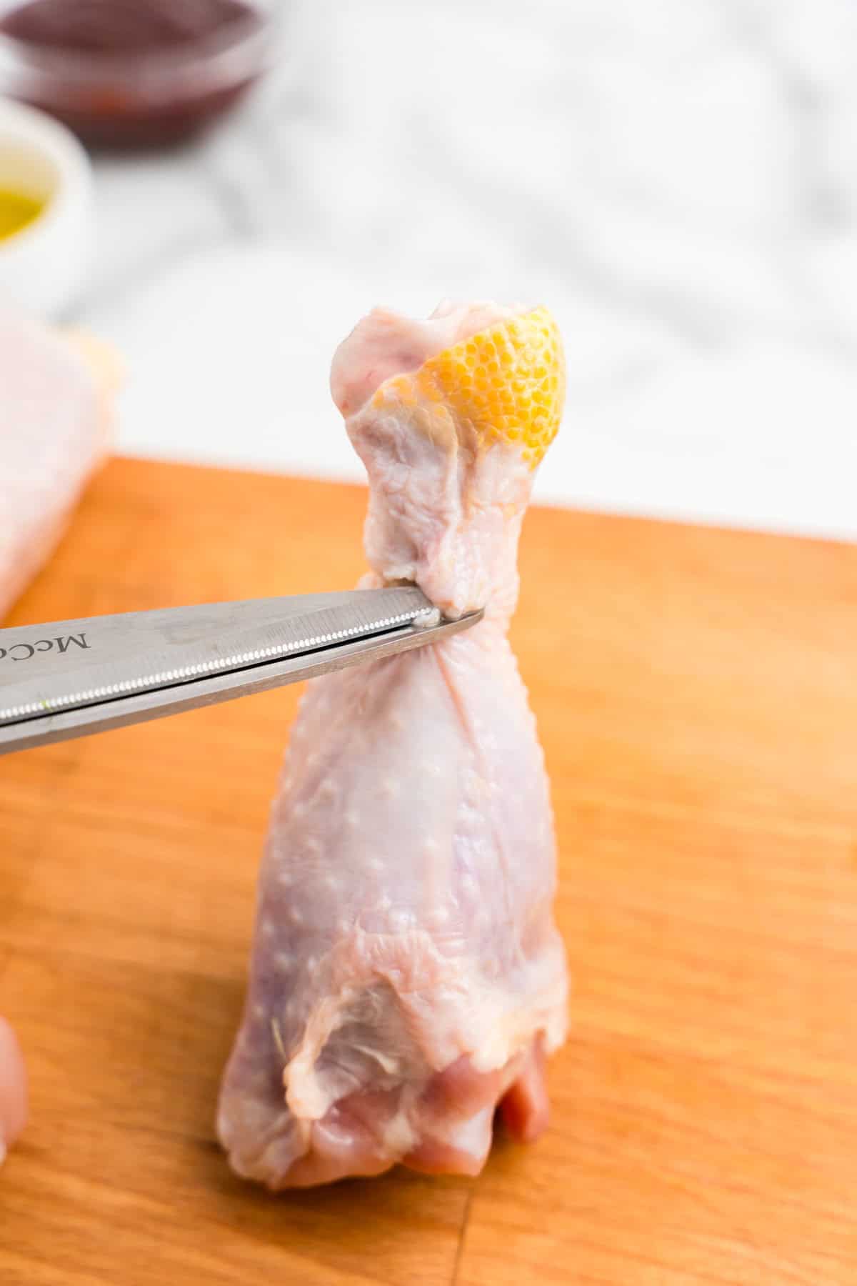 Cutting skin on chicken drumsticks with kitchen shears