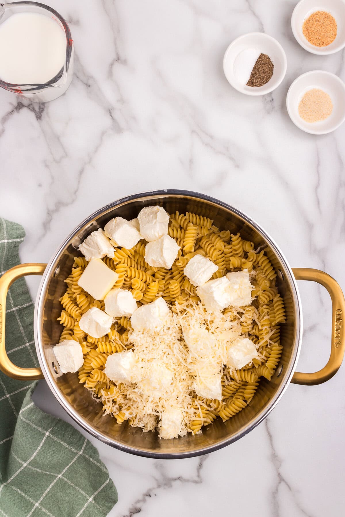 A hand placing a lid on a pot containing pasta, cream cheese, and cheese mixture, preparing it for cooking.