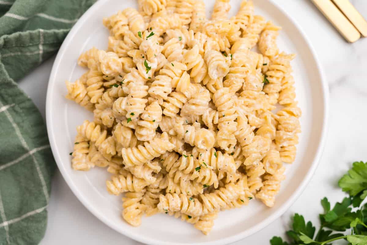 Close-up of a white plate filled with creamy rotini pasta garnished with finely chopped parsley.