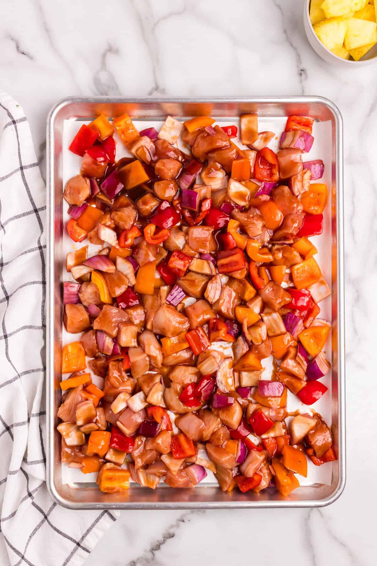 The marinated chicken and vegetables are now spread evenly onto a lined baking sheet, prepared for cooking.