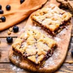 Peanut Butter and Jelly Bars on wood cutting board dusted with powdered sugar.