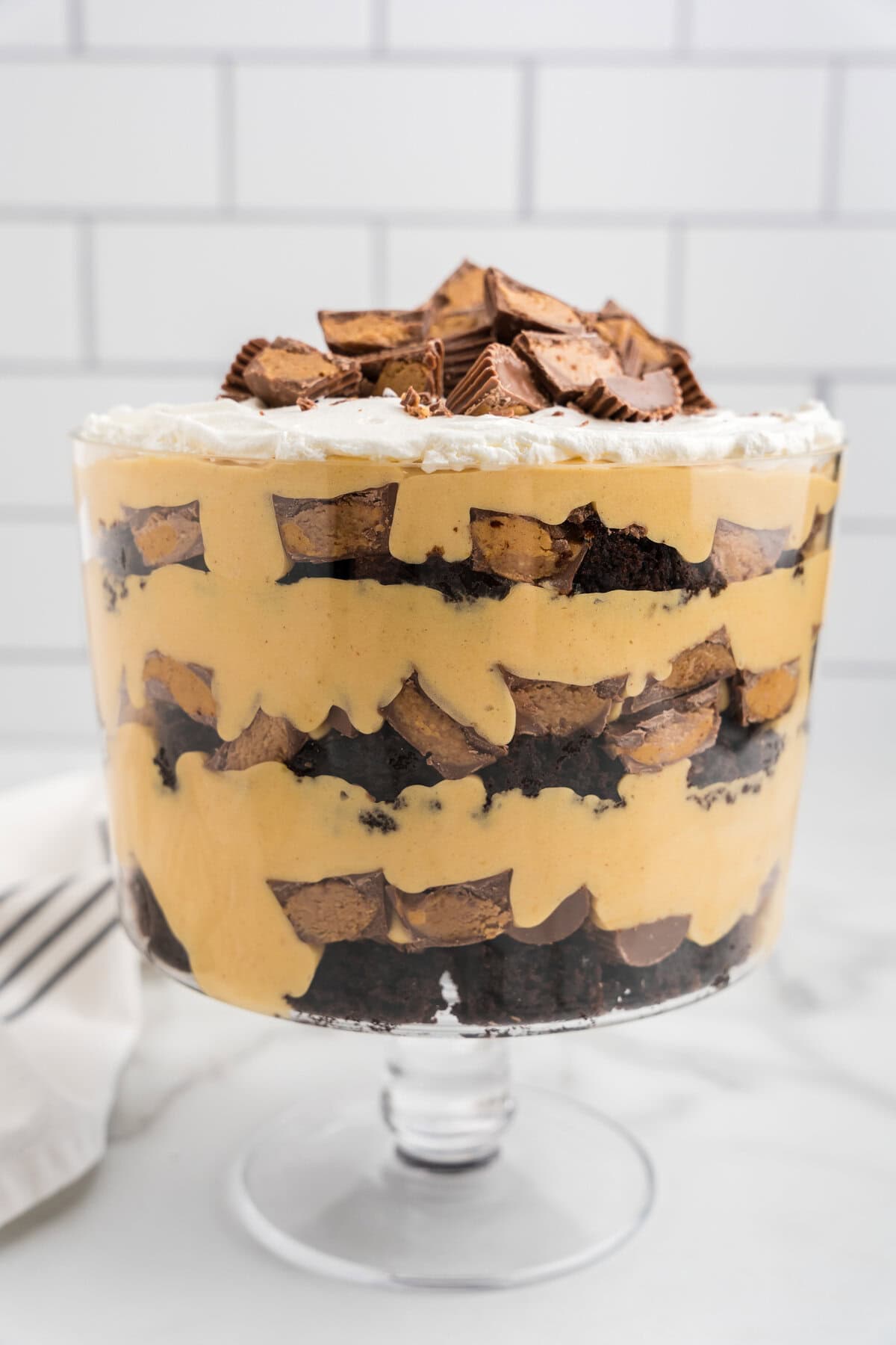 A fully assembled Reese’s Peanut Butter Trifle with layers of brownies, peanut butter filling, and Reese’s cups, topped with whipped cream and more candy.