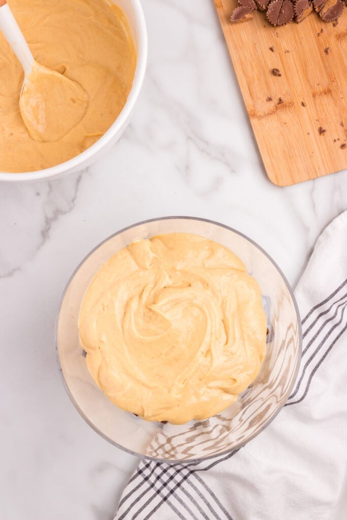 A generous layer of peanut butter cream spread over the brownie and candy base inside the trifle dish.