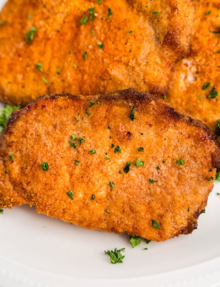 A plate stacked with golden, breaded pork chops, garnished with fresh parsley.