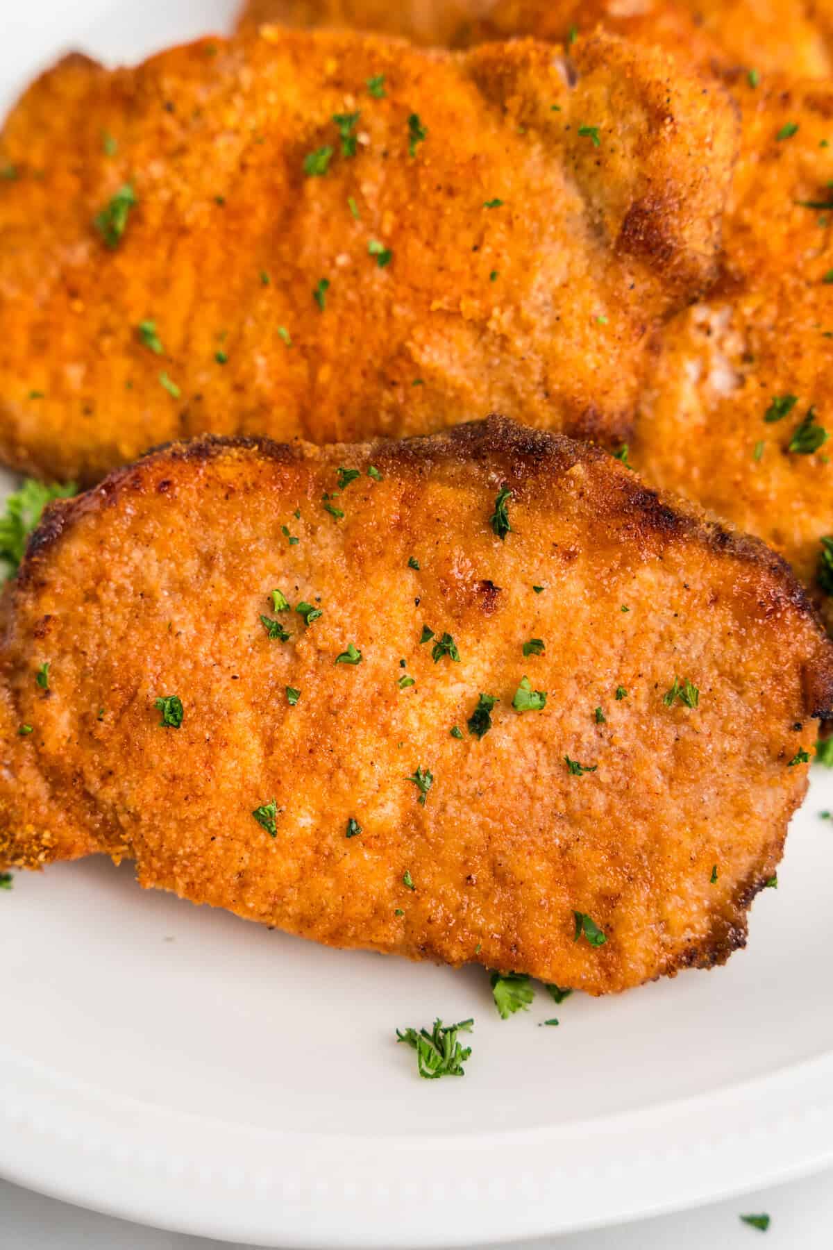 A plate stacked with golden, breaded pork chops, garnished with fresh parsley.
