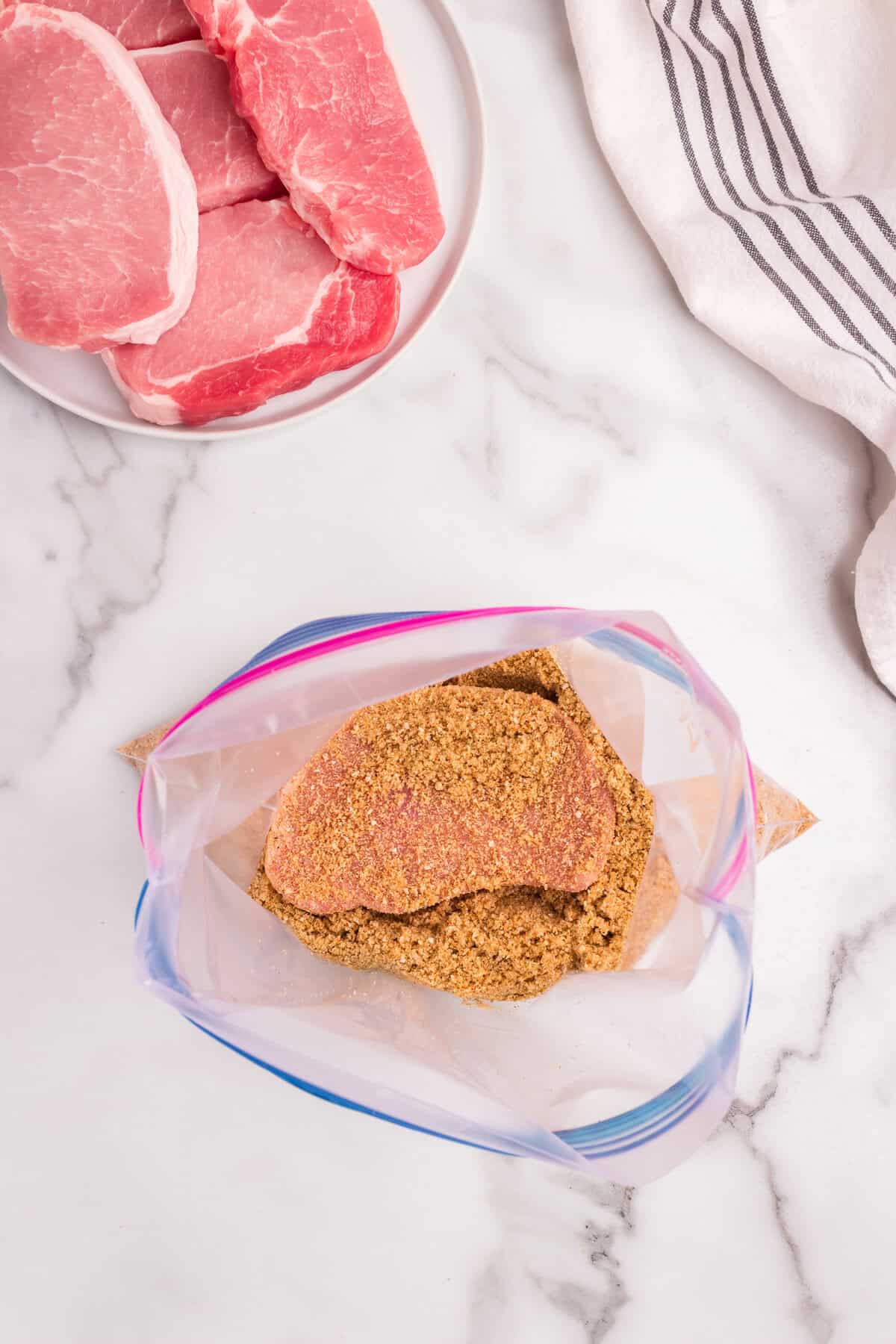 A pork chop fully coated with the breadcrumb mixture inside the plastic bag.