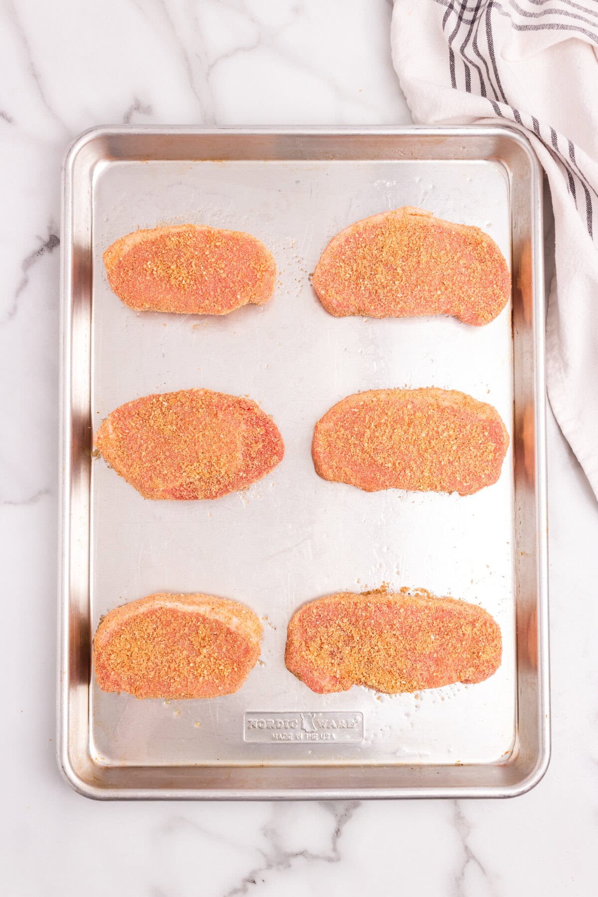 Six breaded pork chops arranged on a baking sheet, ready for cooking.