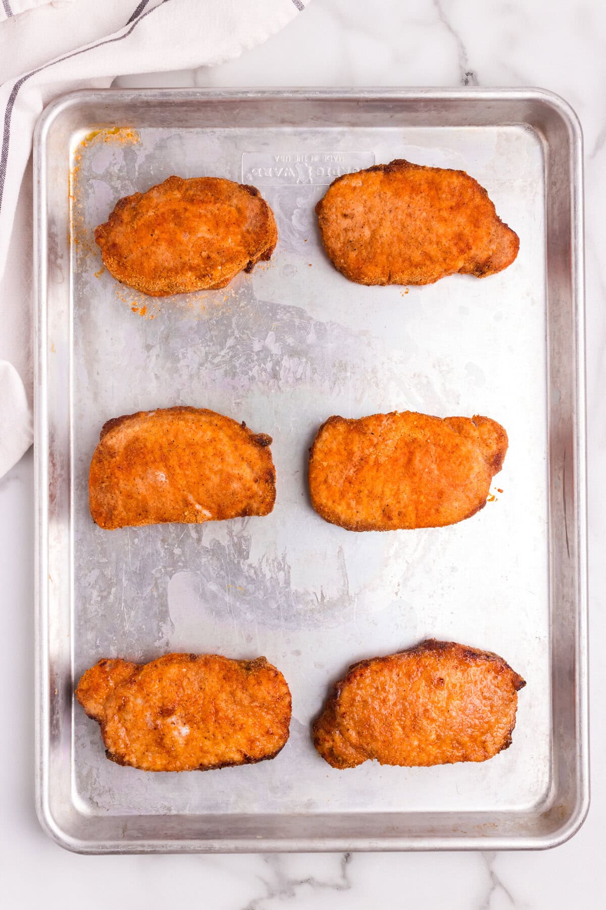 The pork chops after baking, now golden brown and crispy on a baking sheet.