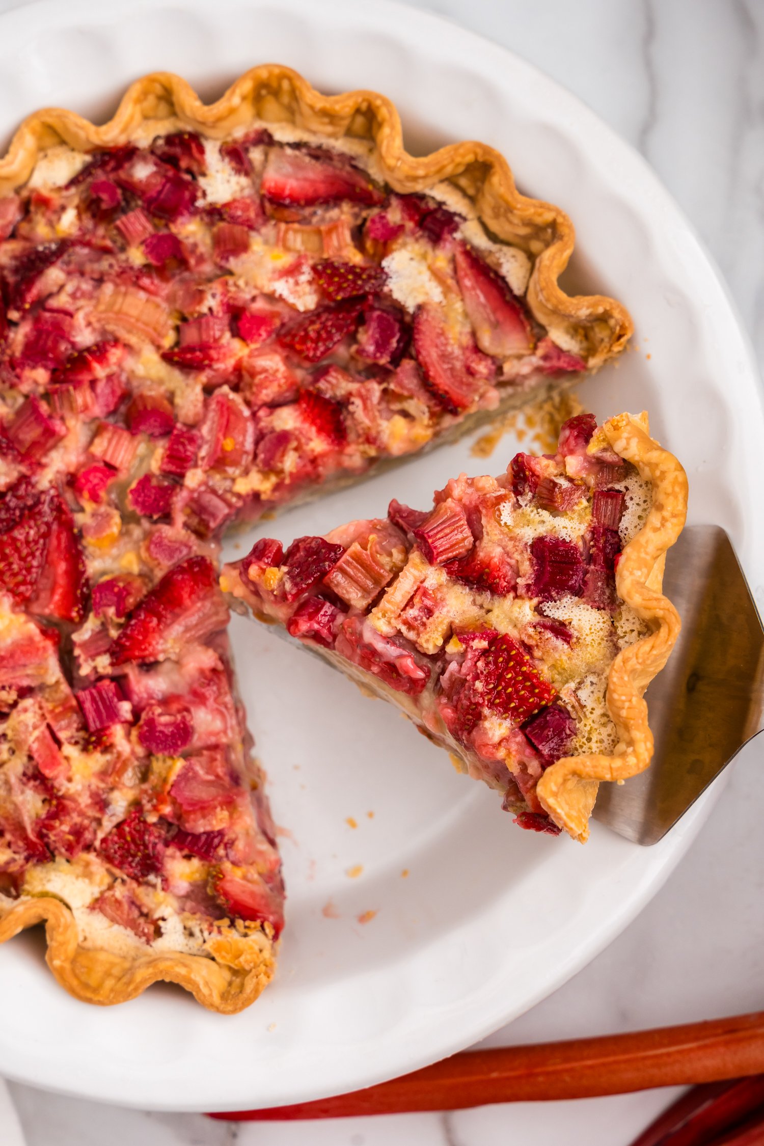 Strawberry Rhubarb Pie cut into slices in pie plate with one slice being removed