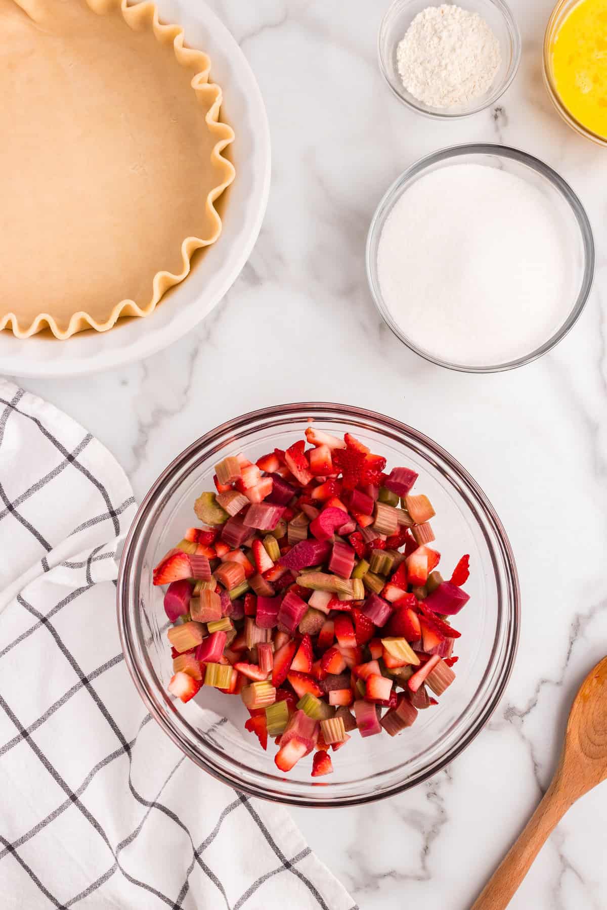 Cut and prepared rhubarb and starwberry pieces tossed in glass mixiing bowl for Strawberry Rhubarb Pie