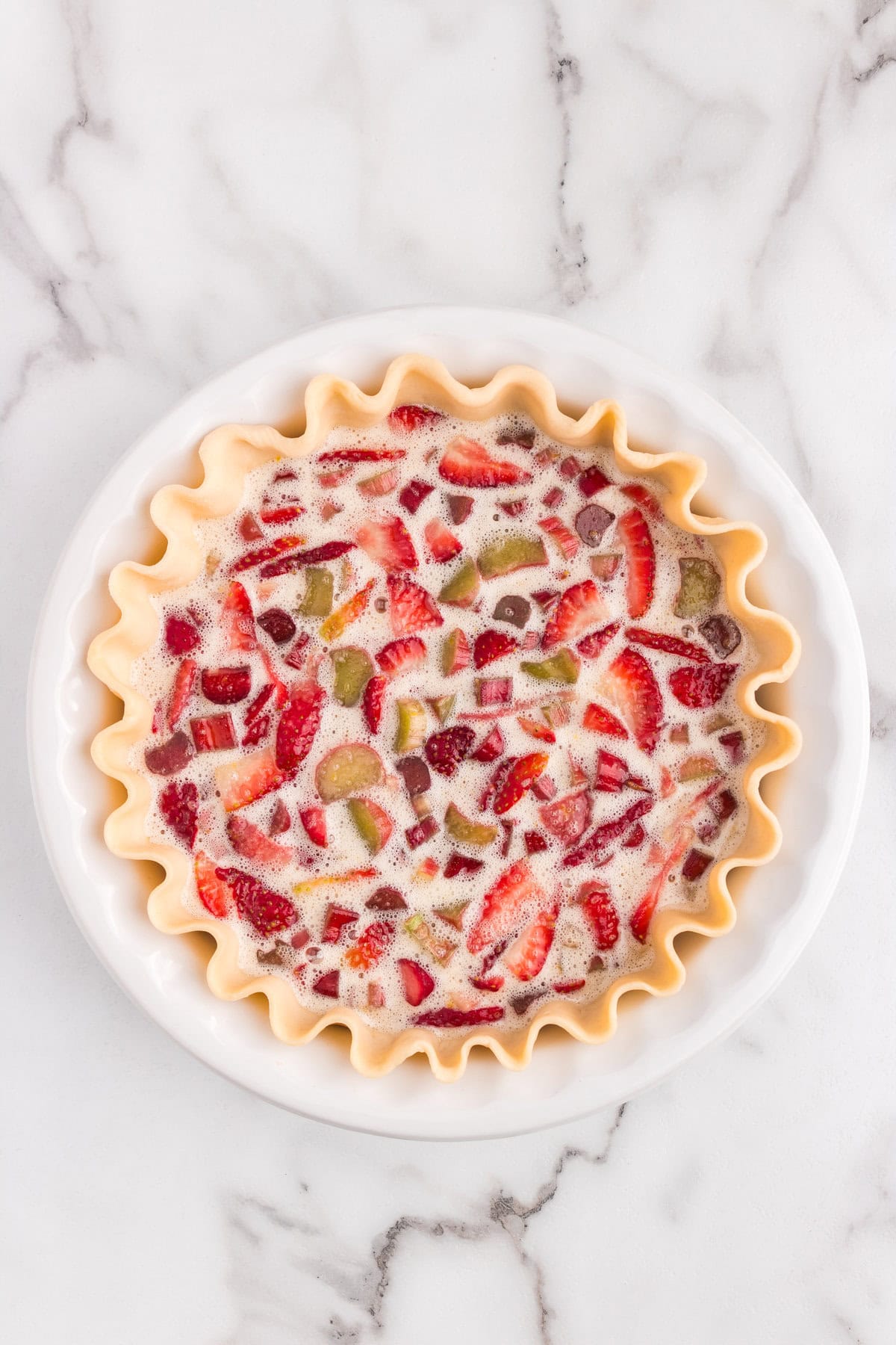 Pouring Strawberry Rhubarb Pie filling into pie shell in pie plate 