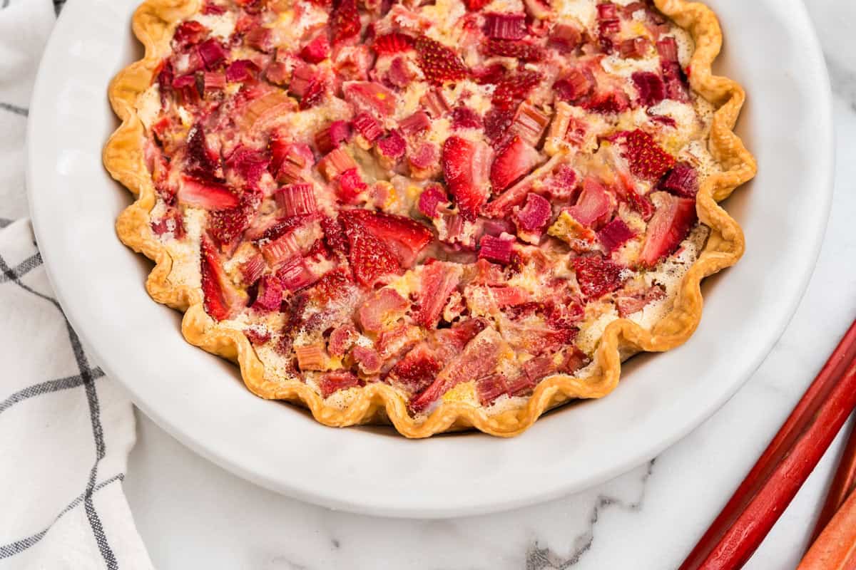 Strawberry Rhubarb Pie in white pie plate ready to be sliced