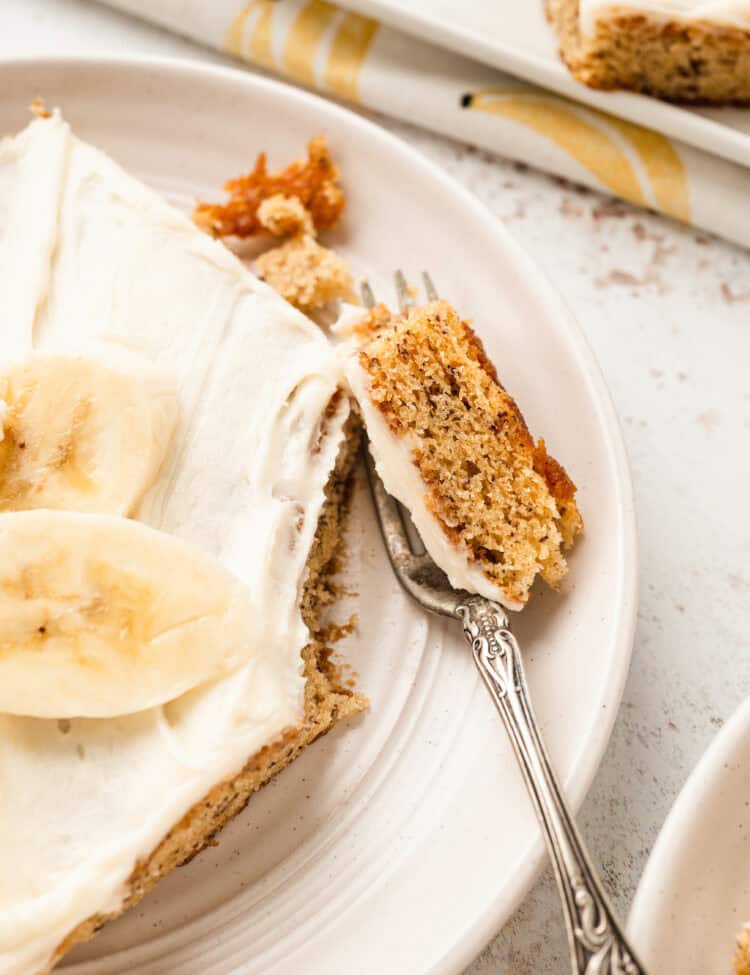 A close-up shot of a banana bar on a plate with a forkful lifted, showing the moist interior and creamy frosting.