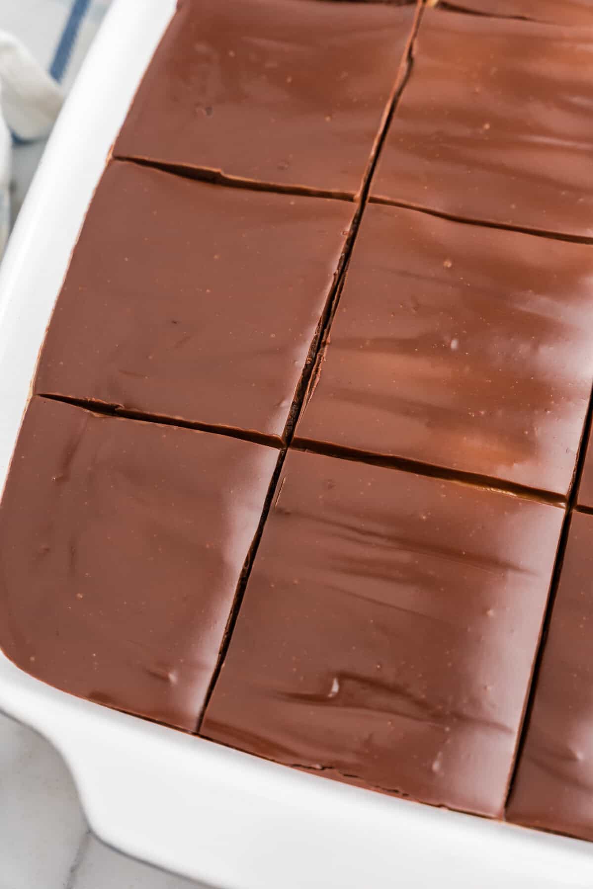 A close-up of the sliced cake in the pan, showing the smooth chocolate ganache top and cake portions beneath.