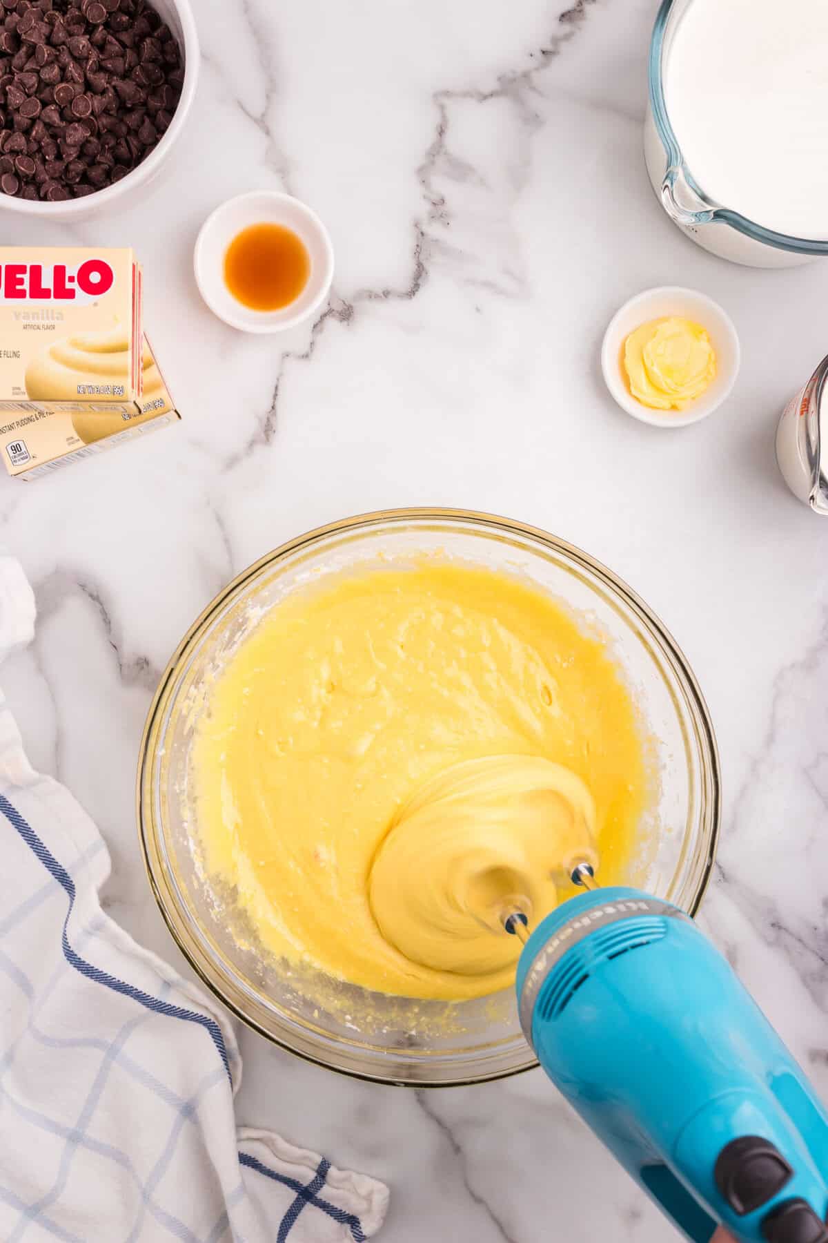 An electric hand mixer blending the cake batter into a smooth yellow mixture in a glass bowl.
