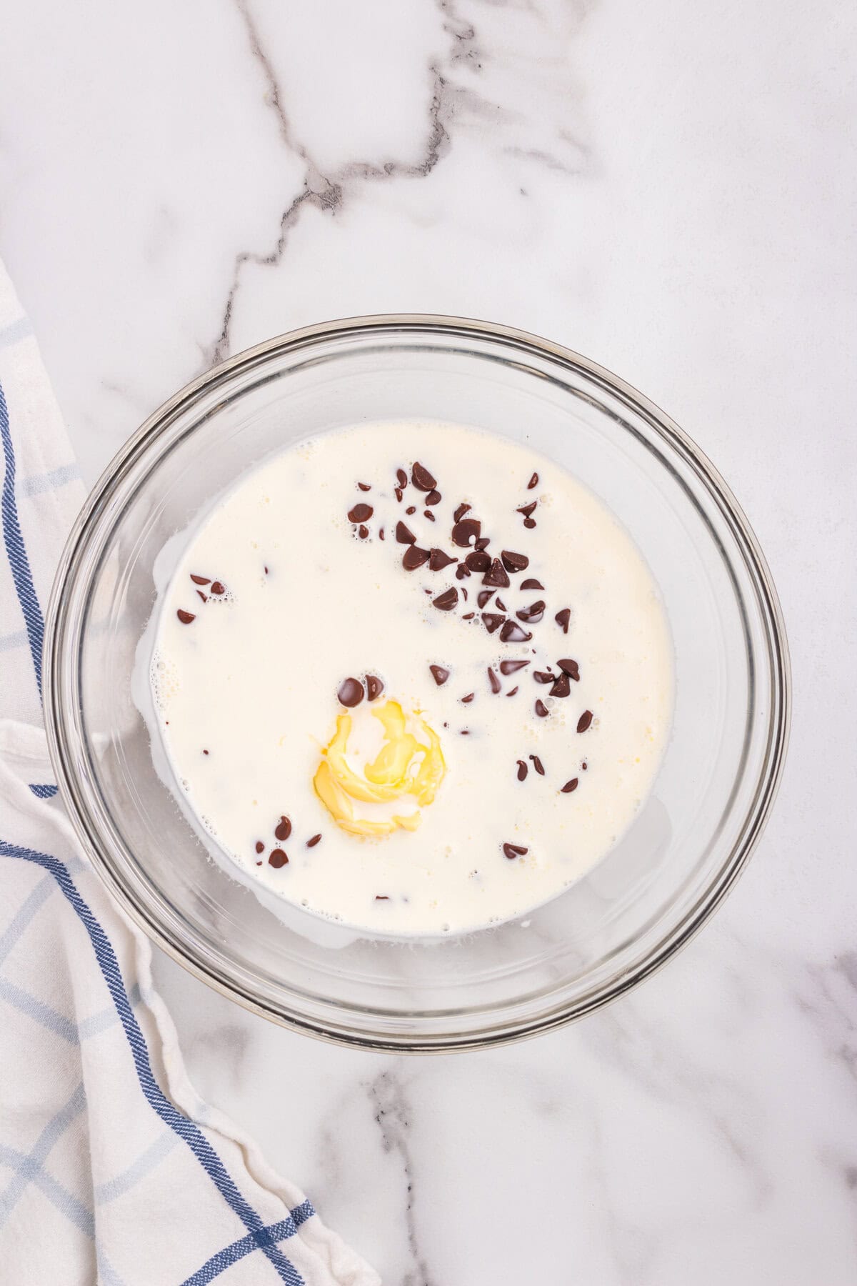 A glass bowl filled with heavy cream, chocolate chips, and a dollop of butter—ingredients for making chocolate ganache.