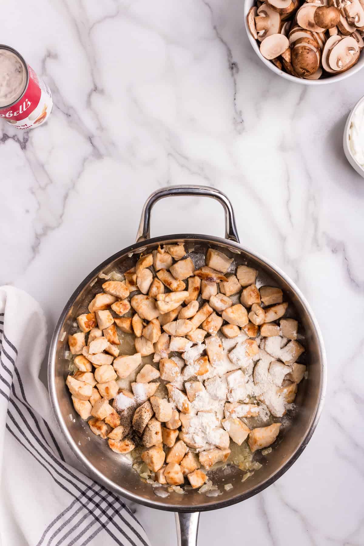 Chicken pieces are browning in the skillet with sautéed onions; flour, salt, and pepper have been sprinkled over the cooked chicken.
