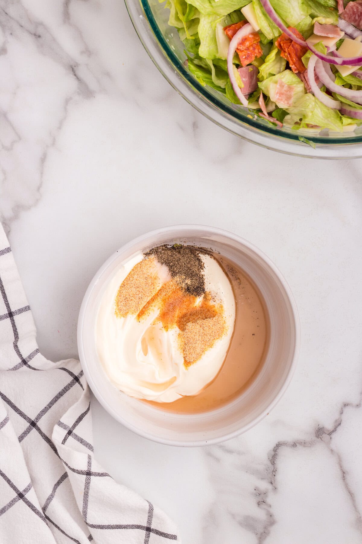 A small bowl containing the ingredients for the salad dressing—mayonnaise, vinegar, garlic powder, black pepper, and other seasonings—before mixing.