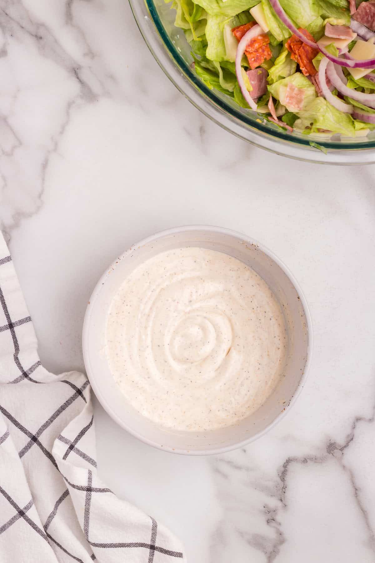 A small bowl of creamy, well-mixed salad dressing with visible flecks of seasoning, ready to be added to the salad.