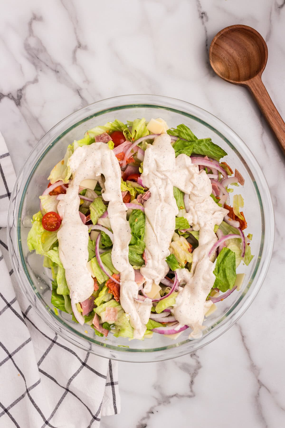 The assembled salad in a large glass bowl with the creamy dressing drizzled generously over the top, not yet mixed in.
