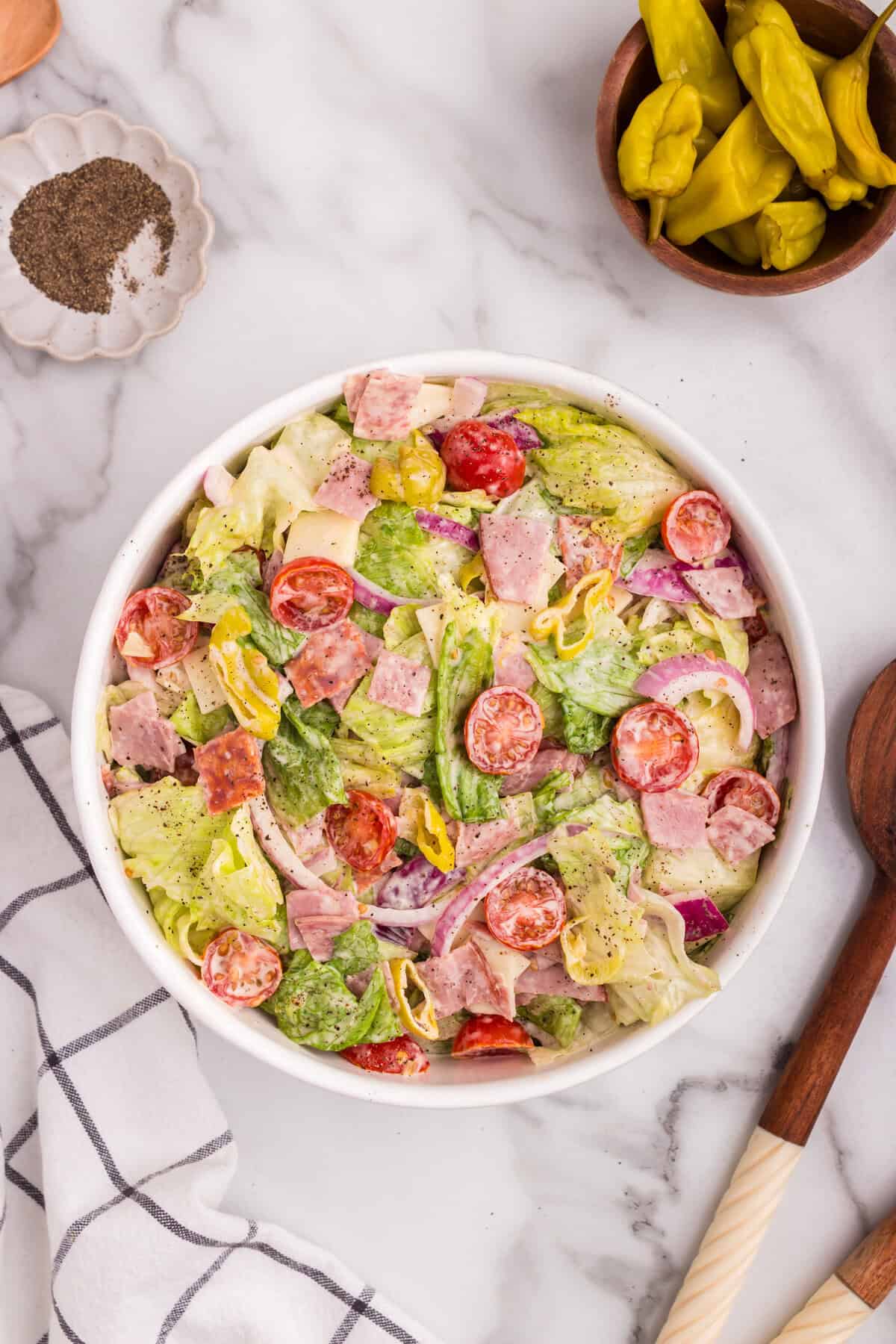 The completed grinder salad served in a white bowl, garnished with freshly ground black pepper and additional banana peppers for presentation.